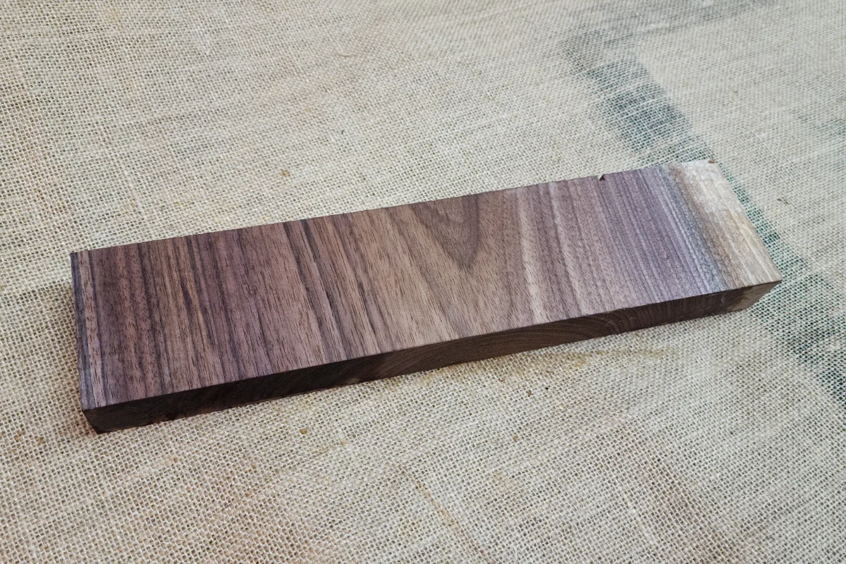 Bloco rectangular liso de nogueira escura com veio direito, pousado em juta